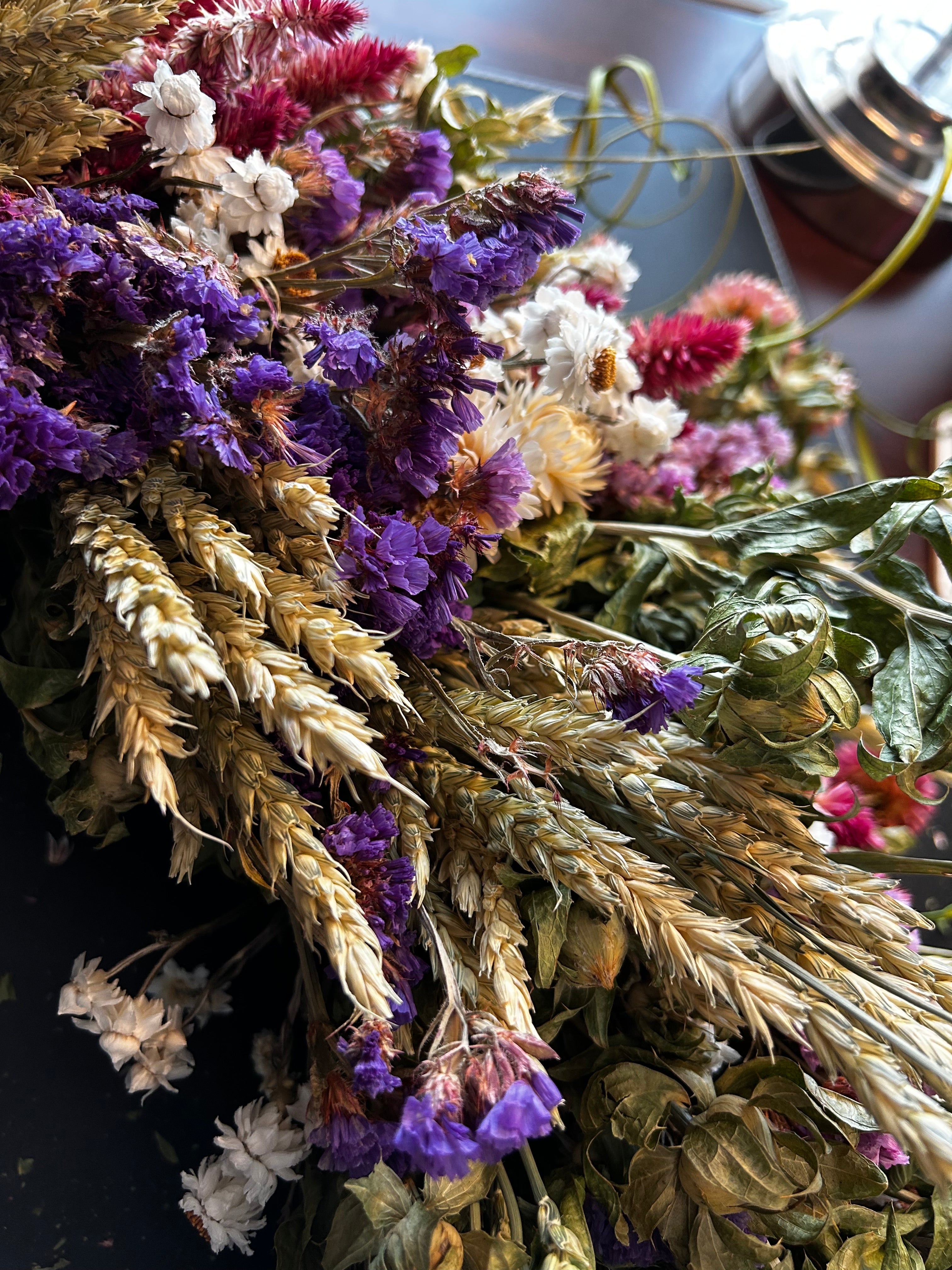 Close-up of decorative 30 inch dried floral wreath with vibrant statice and helichrysum and the whimsical texture of various grains, and curly ting ting on a dark background