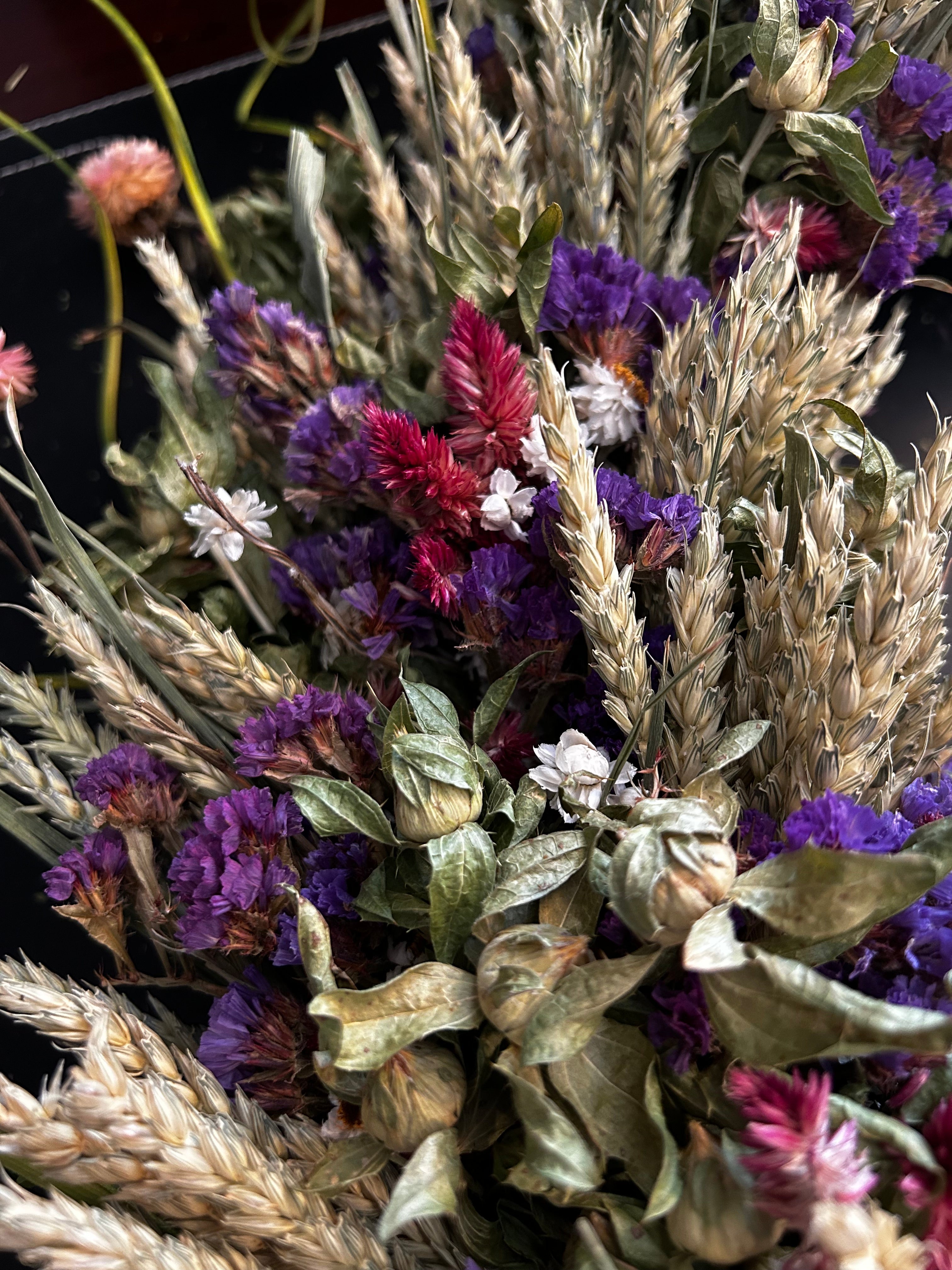 Close-up of decorative 30 inch dried floral wreath with vibrant statice and helichrysum and the whimsical texture of various grains, and curly ting ting on a dark background