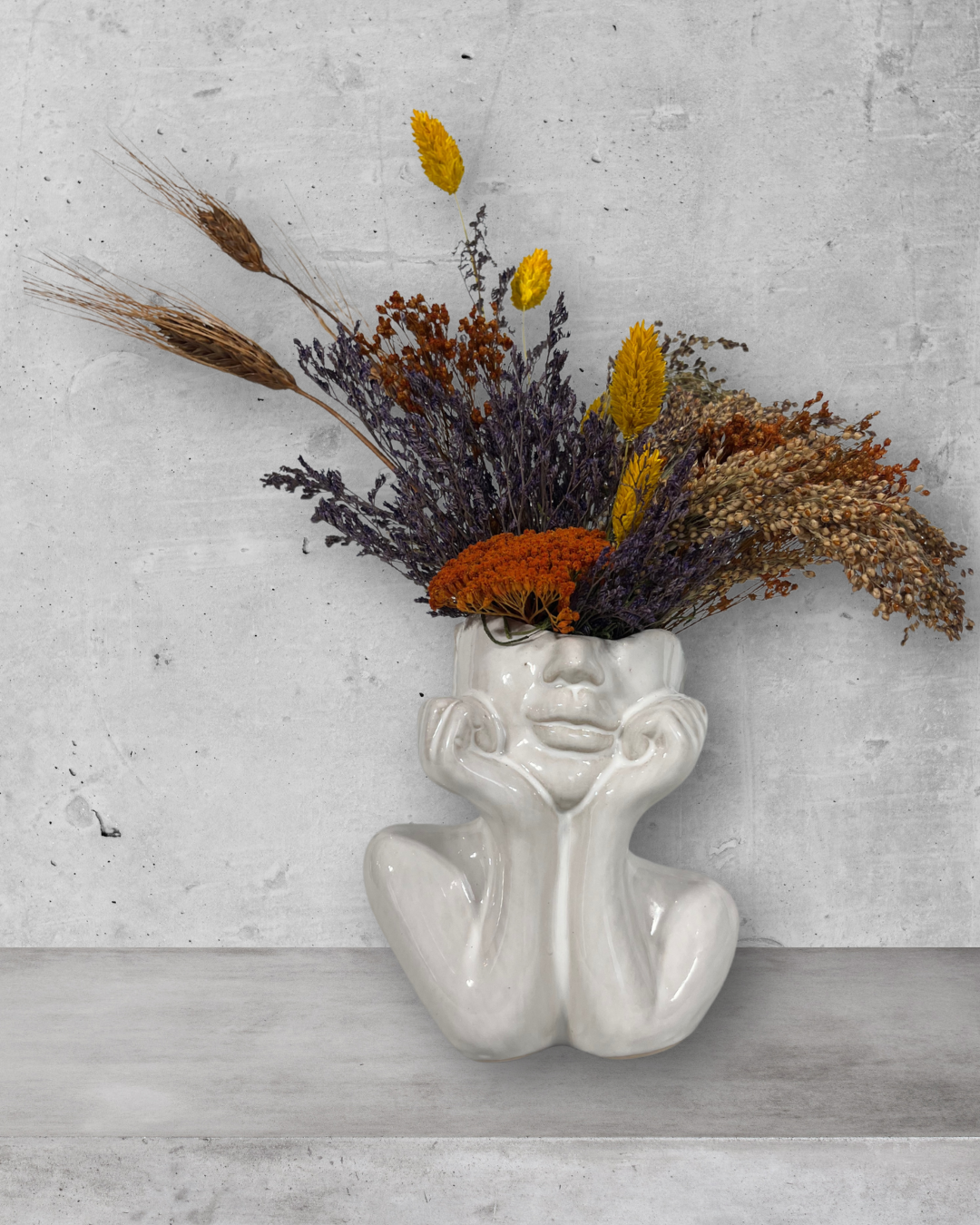 Decorative vase shaped like a face with dried flowers on a gray surface