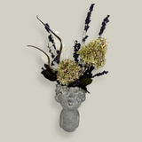 Decorative everlasting flower arrangement in a concrete vase sculpted as a woman's serene face with her lips charmingly puckered.