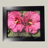 Matte black framed artwork of pink hibiscus flowers on a green leafy background