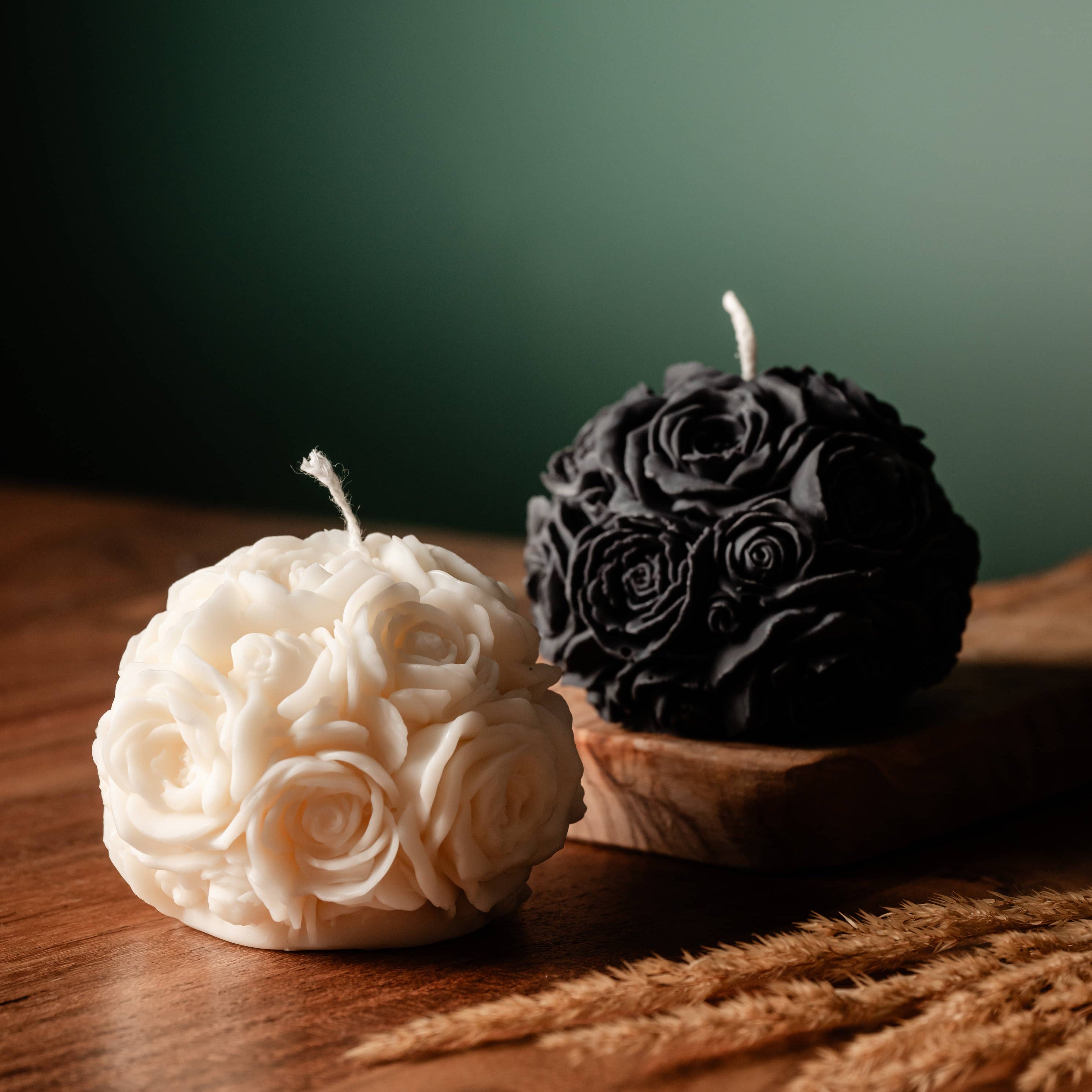 A white and a black spherical soy wax candles embossed with a beautiful rose motif on a wooden surface.
