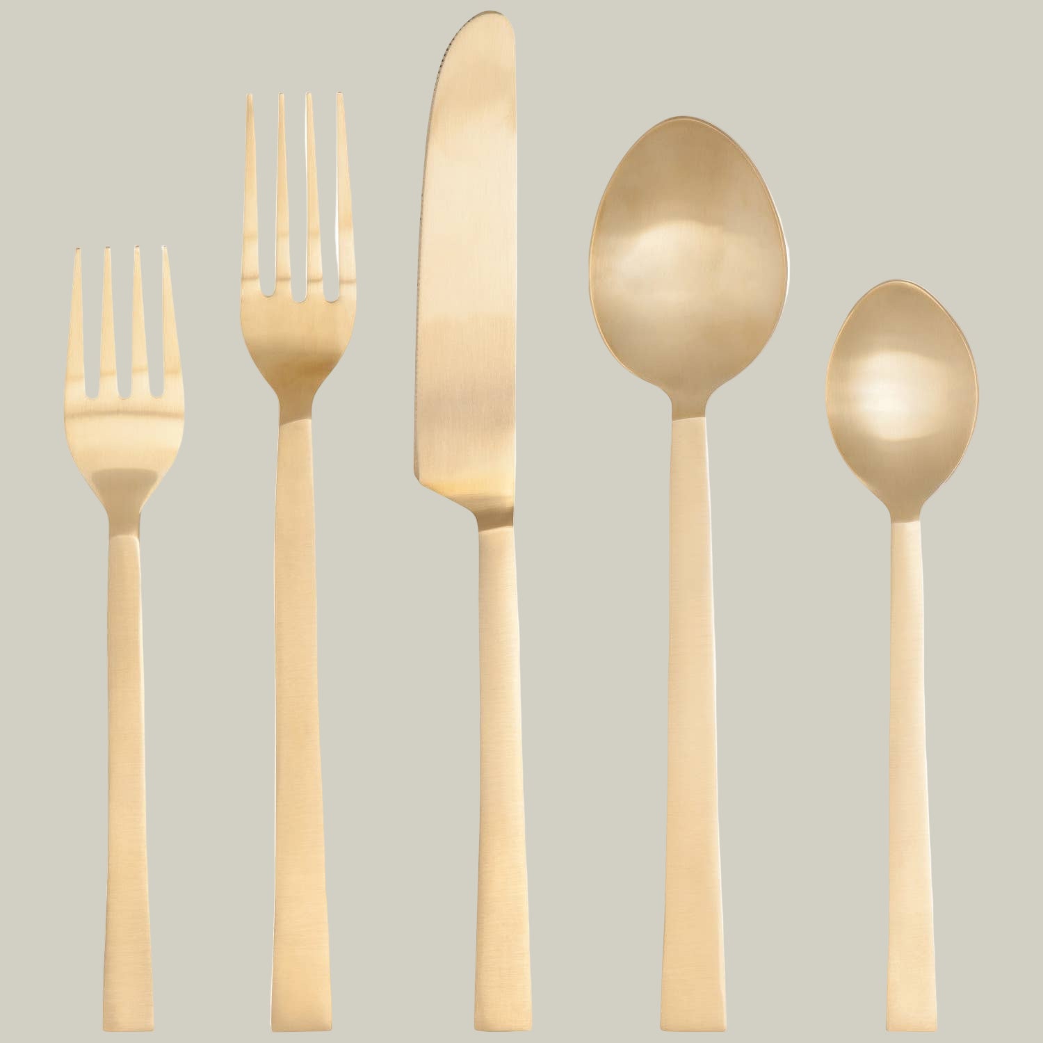Set of gold plated stainless steel cutlery including two forks, a knife, and two spoons on a soft green background.