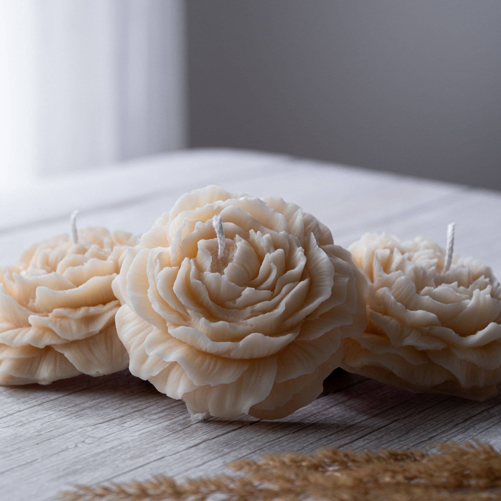 Three beautiful small candles in the shape of a peony flower placed on a wooden surface. 