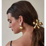 Woman with a gold hair accessory and earrings on a neutral background