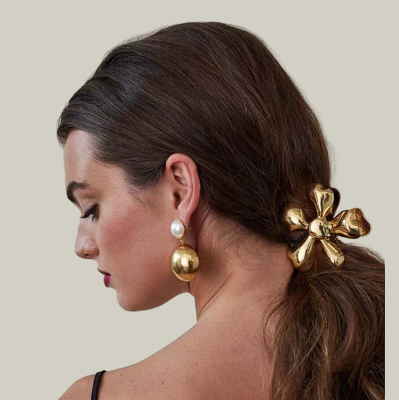 Woman with a gold hair accessory and earrings on a neutral background