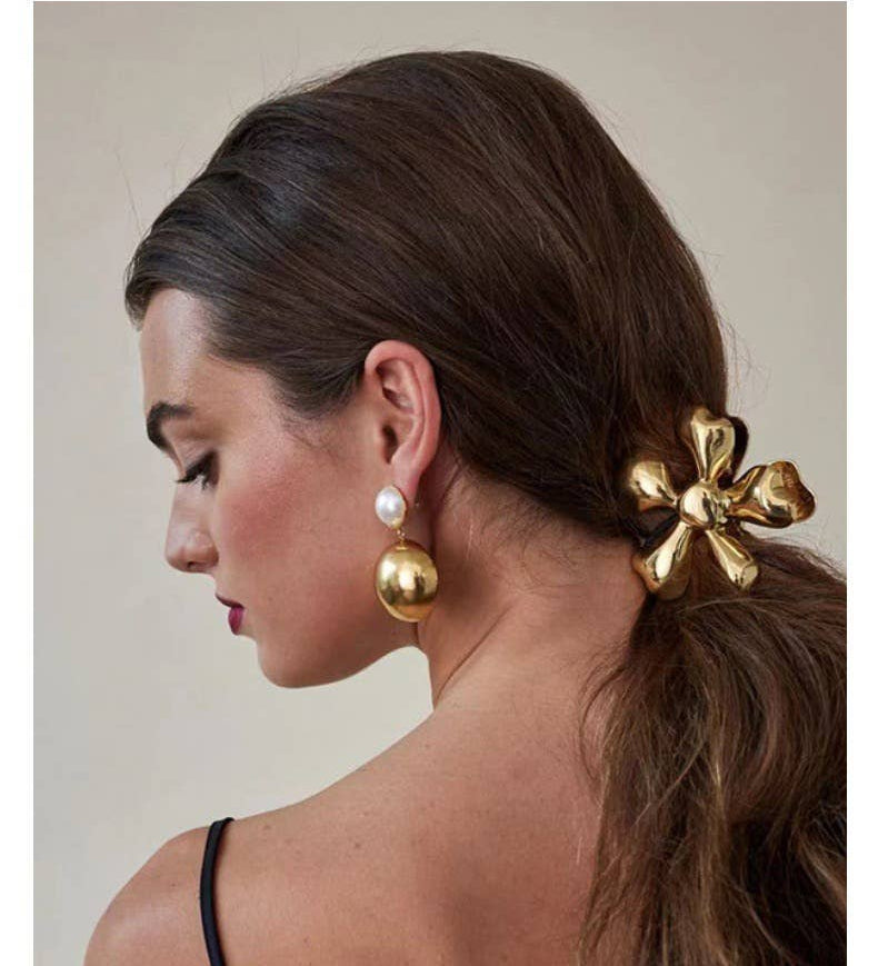 Woman with a gold hair accessory and earrings on a neutral background