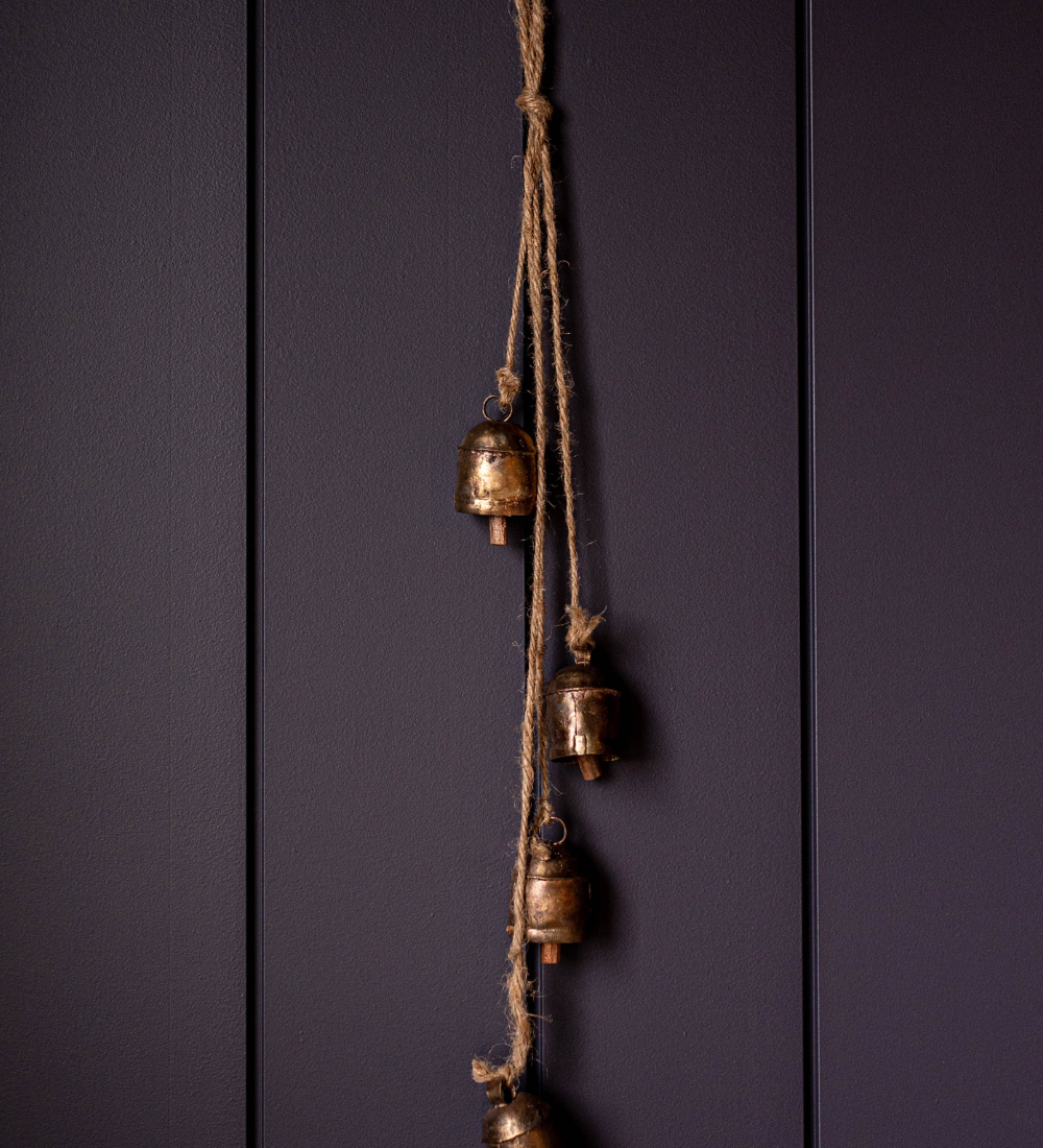 Four brass bells hanging on a rope against a dark wooden panel background
