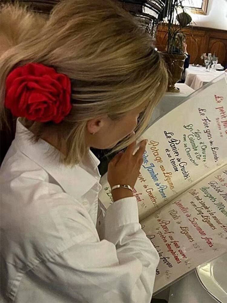 Person with a red flower clip in their hair looking at a menu in a restaurant.