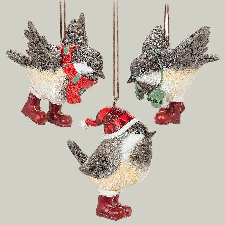Three decorative winter chickadee ornaments wearing red boots, one has green mittens on a string around it's neck, the second has a red scarf around it's neck, and the third is wearing a red hat.