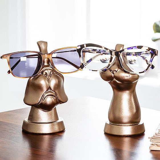 Bronze coloured eye glass holders. One is shaped like the lower portion of a dog's face, whose name is Barnaby. The other is shaped like the lower portion of a cat's face, whose name is Cleo. 