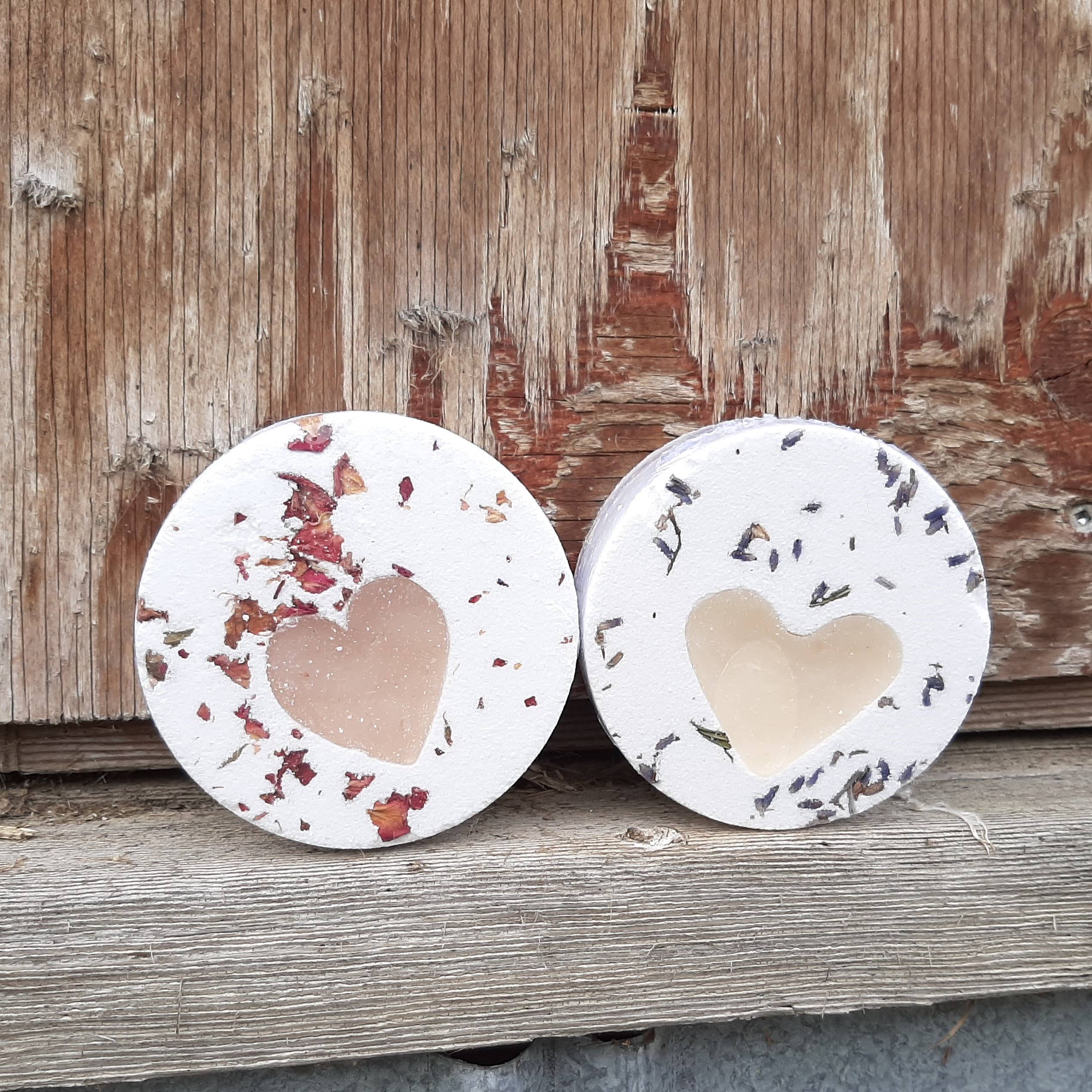 Two round bath balms with rose petals and lavender and heart shaped soap centres on a wooden surface