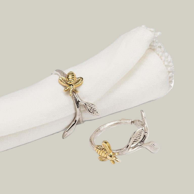 Gold and silver bee-shaped napkin rings on a white napkin.