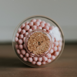 Blush pink match jar with cork lid on a wooden surface and gray background