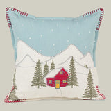 Decorative pillow with a winter scene featuring a red cabin, trees, and mountains.