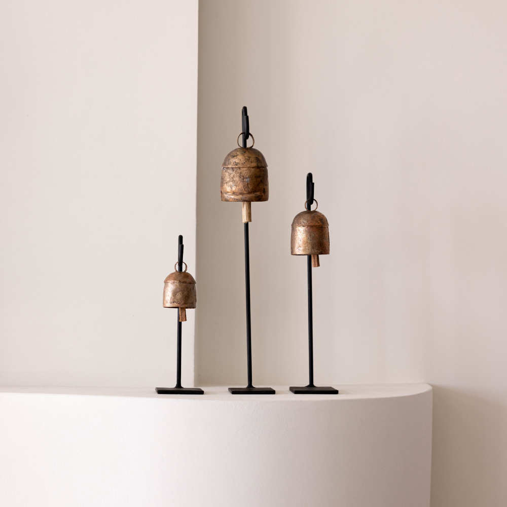 Set of three bronze-colored decorative bells on a white pedestal against a plain wall.