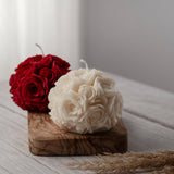 Two spherical soy wax candles embossed with a beautiful rose motif on a wooden surface. One of the candles is white and the other is red.