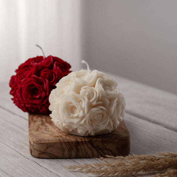 Two spherical soy wax candles embossed with a beautiful rose motif on a wooden surface. One of the candles is white and the other is red.