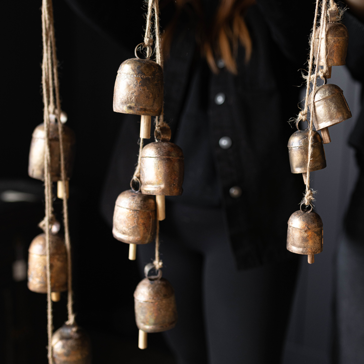Three sets of vintage inspired bronze coloured hanging bells being held up by a person against a dark background