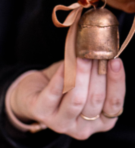 Hand holding a small bronze bell with a ribbon against a dark background