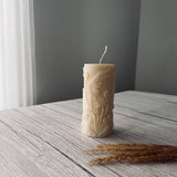 Decorative white pillar candle embossed with fern pattern on a wooden surface