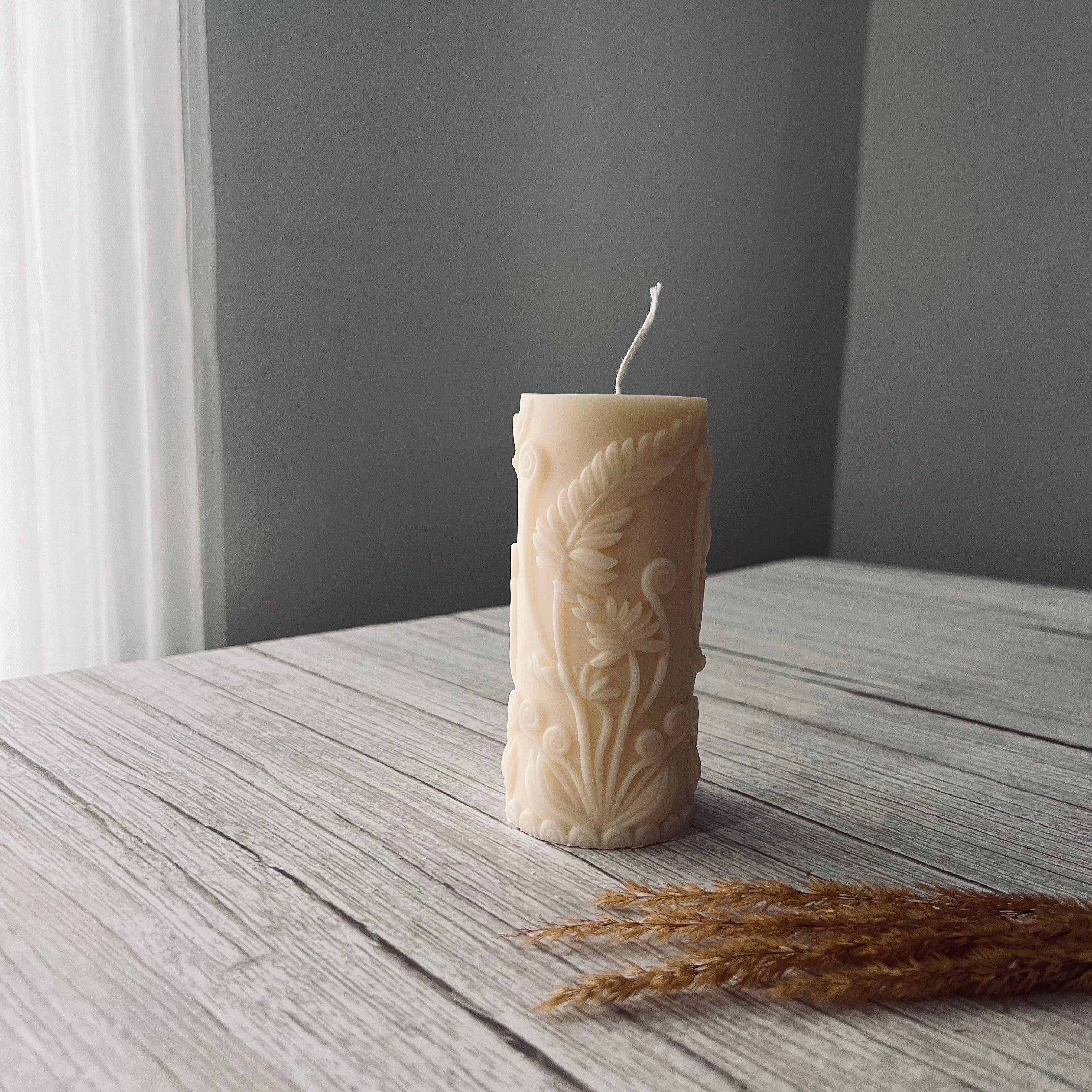 Decorative white pillar candle embossed with fern pattern on a wooden surface