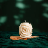 White rose-shaped candle on a wooden stand against a dark green background