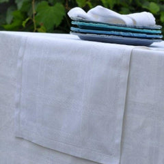 Stack of plates on a white tone on tone patterned napkin with matching table runner set outdoors 