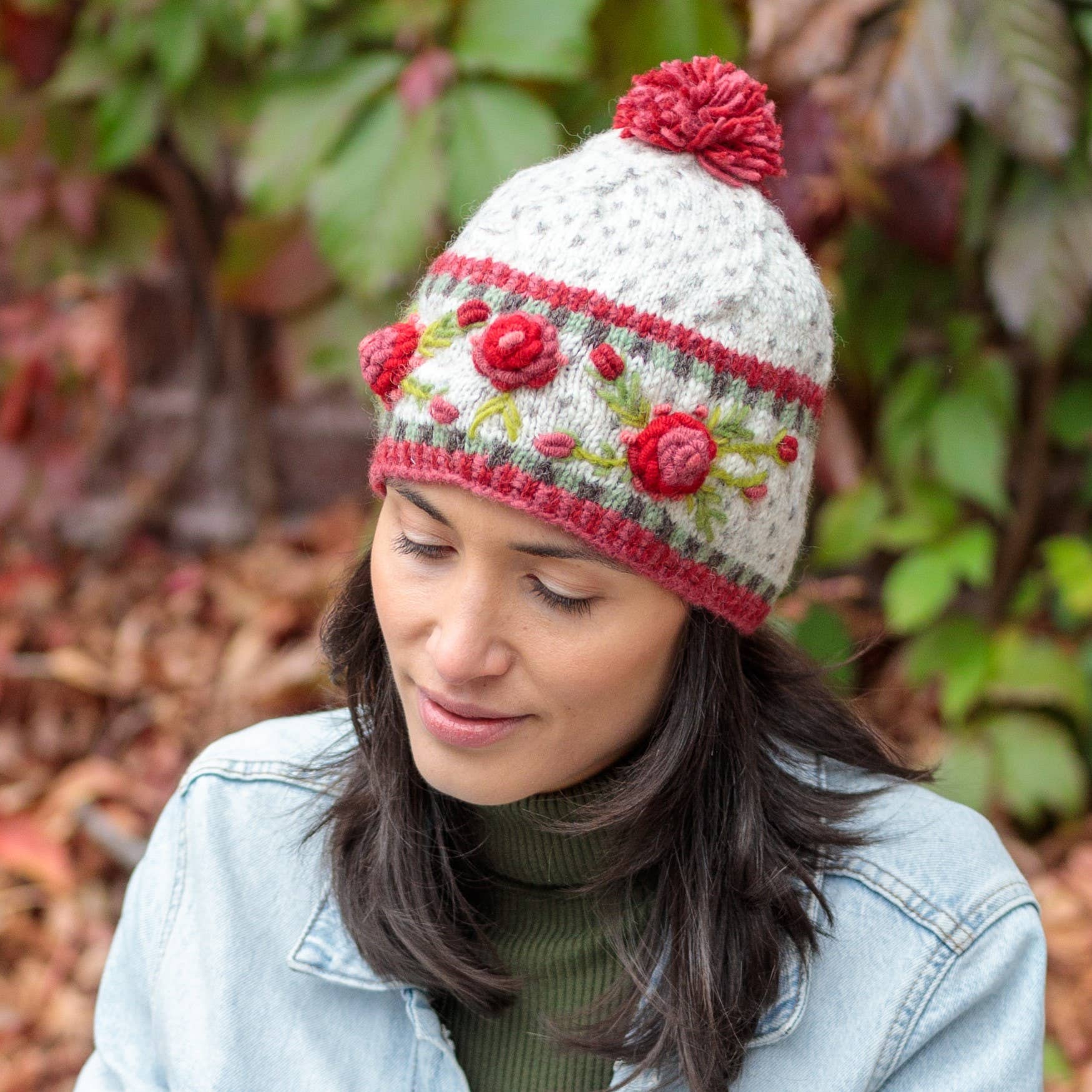 Woman wearing a hand-knit floral-patterned knit hat in an outdoor setting with greenery.