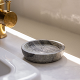 Grey marble textured soap dish on a white sink with a gold faucet.