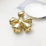 Gold bow-shaped hair clip on a white surface with a magazine in the background