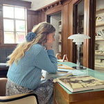 Woman wearing a blue floral hair clip sitting at a desk in a room with wooden paneling and books.