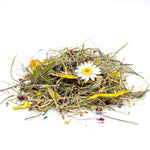 A small pile of dried botanical ingredients, including green grass-like stems, yellow pieces, and a white daisy flower, photographed on a clean white background. 2