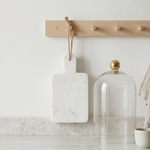 Decorative items including a marble cutting board, glass dome, and small bowl on a marble surface with a wooden pegboard in the background.