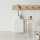 Decorative items including a marble cutting board, glass dome, and small bowl on a marble surface with a wooden pegboard in the background.