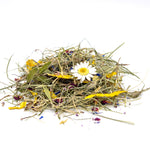 A small pile of dried botanical ingredients, including green grass-like stems, yellow pieces, and a white daisy flower, photographed on a clean white background. 2
