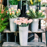 Floral arrangements in metal buckets on a wooden table with a blurred indoor background