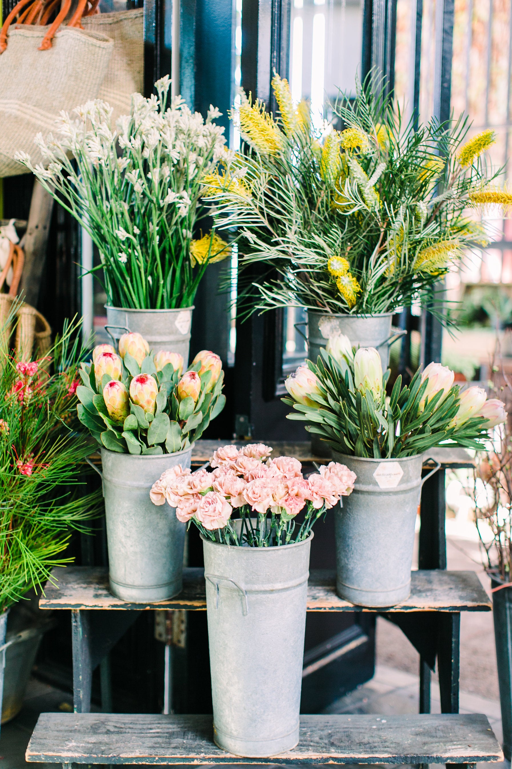 Floral arrangements in metal buckets on a wooden table with a blurred indoor background