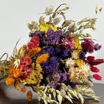 This magnificent, hand-tied bouquet is a vibrant symphony of contrasting colours and textures designed for the sophisticated interior. The Amethyst base of lush purple Statice provides a dramatic backdrop for the Gold accents: bright yellow Achillea Parker and soft natural pink Helichrysums. Textural elements featuring the unique, wavy shapes of red coral Celosia and Phalaris dyed in three complementary colors (natural, orange, and red).