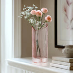 Blush heart shaped glass vase with flowers on a white mantel next to a framed picture