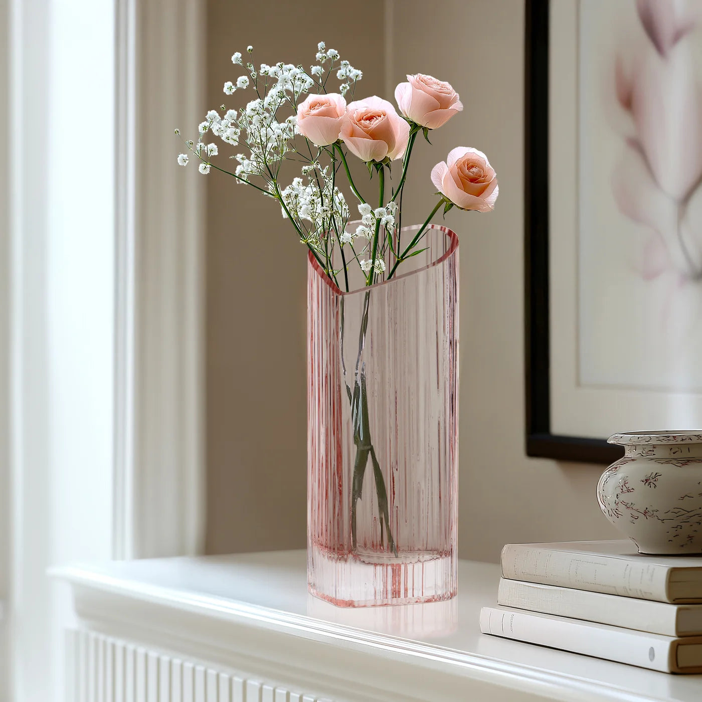 Blush heart shaped glass vase with flowers on a white mantel next to a framed picture