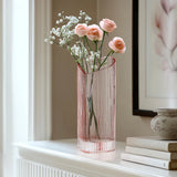 Blush heart shaped glass vase with flowers on a white mantel next to a framed picture