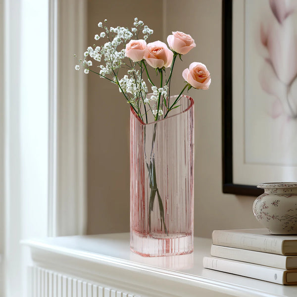 Blush heart shaped glass vase with flowers on a white mantel next to a framed picture