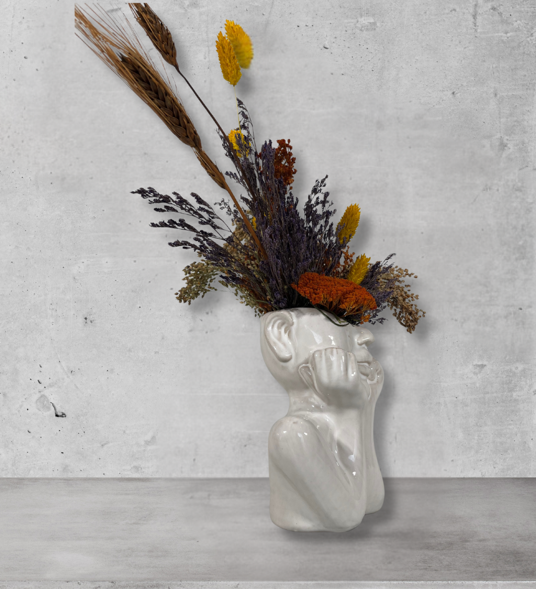 White ceramic vase shaped like a face with dried flowers on a gray concrete background