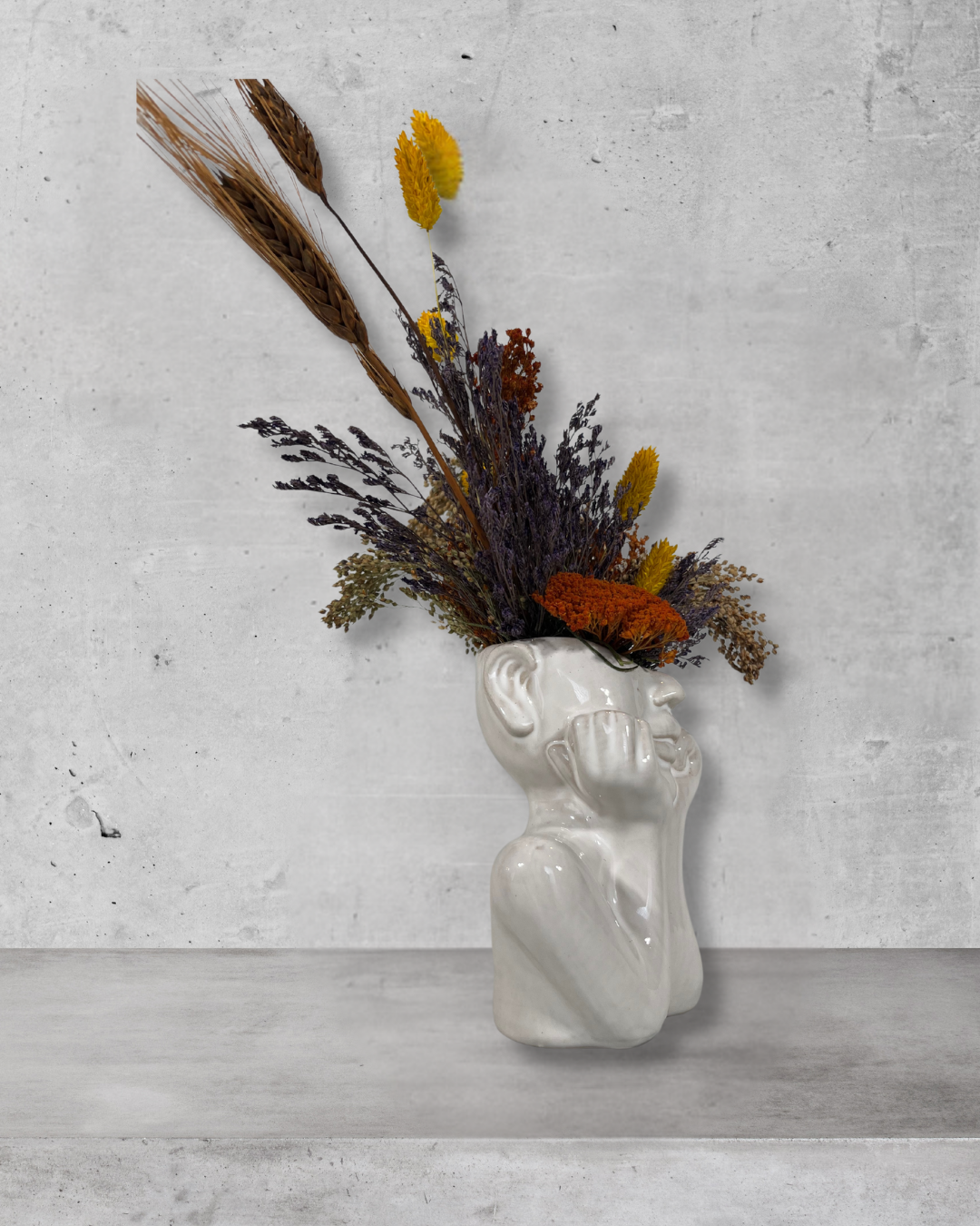White ceramic vase shaped like a face with dried flowers on a gray concrete background