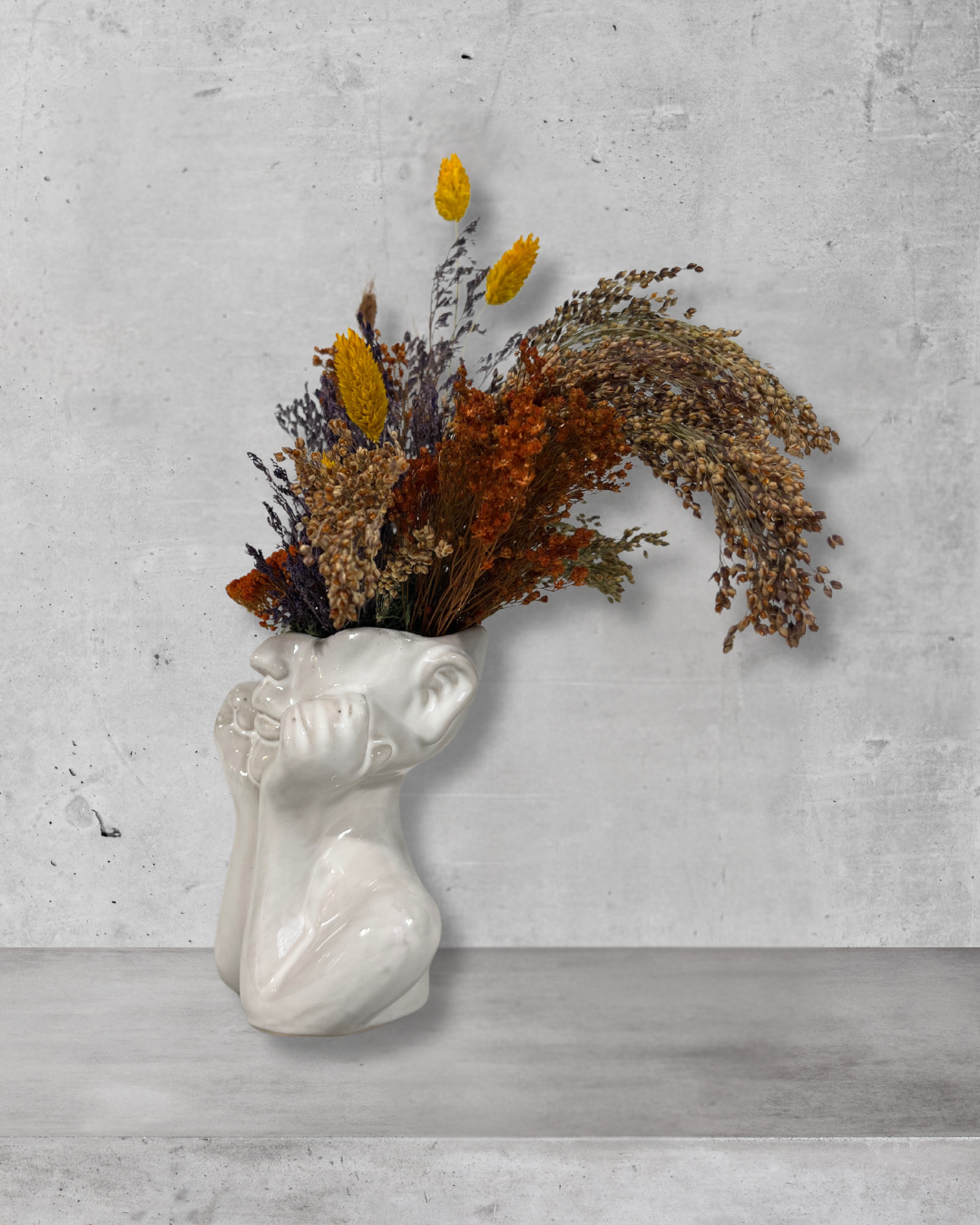 Decorative vase shaped like a human head with dried flowers against a gray concrete wall.