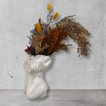Decorative vase shaped like a human head with dried flowers against a gray concrete wall.
