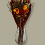 Bouquet titled "Autumn Ember Bouquet" is designed to be a magnificent focal point, perfect for a large vase on a dining table, an entryway, or a mantelpiece. In this photo it is in a clear glass vase with a plain green background.