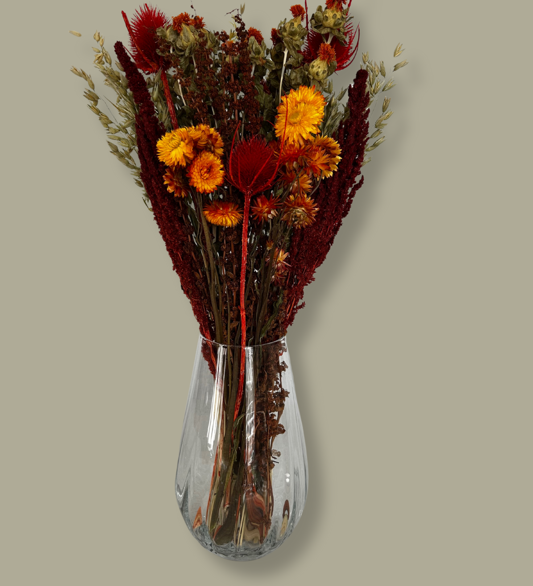 Bouquet titled "Autumn Ember Bouquet" is designed to be a magnificent focal point, perfect for a large vase on a dining table, an entryway, or a mantelpiece. In this photo it is in a clear glass vase with a plain green background.
