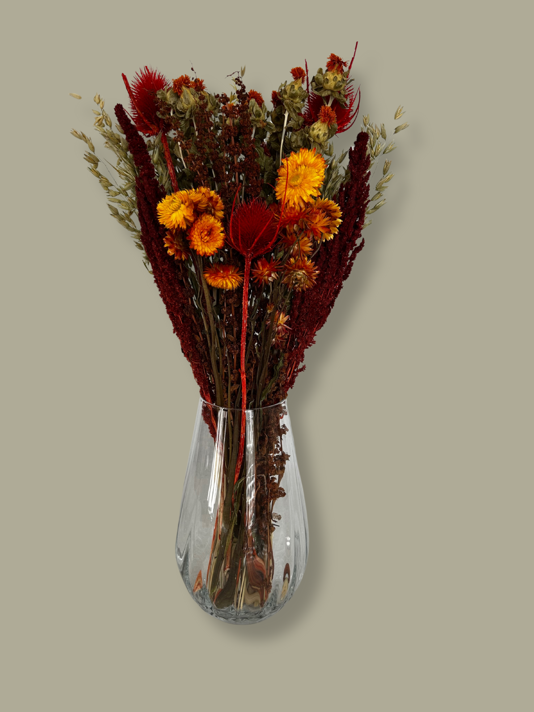 Bouquet titled "Autumn Ember Bouquet" is designed to be a magnificent focal point, perfect for a large vase on a dining table, an entryway, or a mantelpiece. In this photo it is in a clear glass vase with a plain green background.